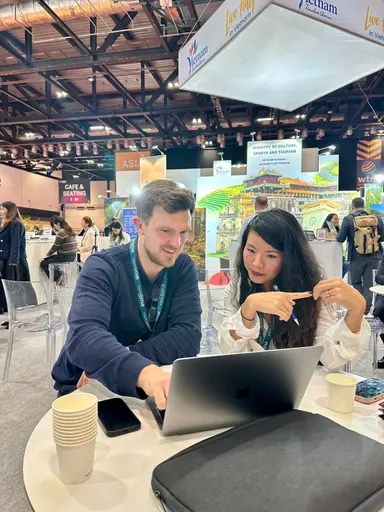 Two of the OpenVoy team working through a travel request on a laptop at a travel trade show.